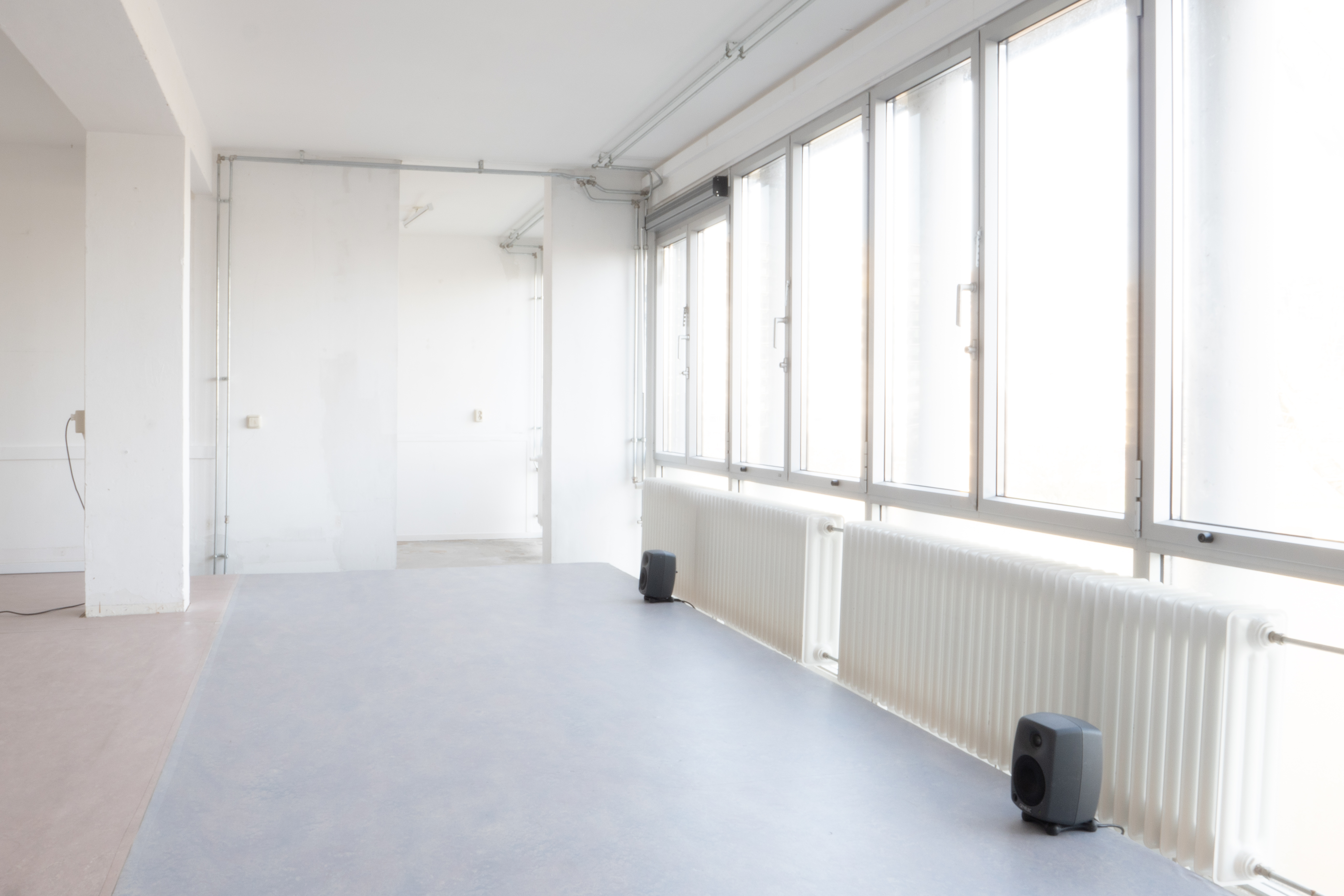 two speakers against a wall of windows and radiators